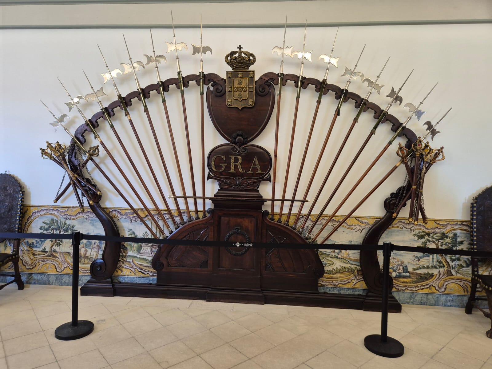 תצוגת נשקים טקסיים באוניברסיטת קוימברה, פורטוגל – מסודרים בצורת מניפה, מתחת לסמל המלכותי