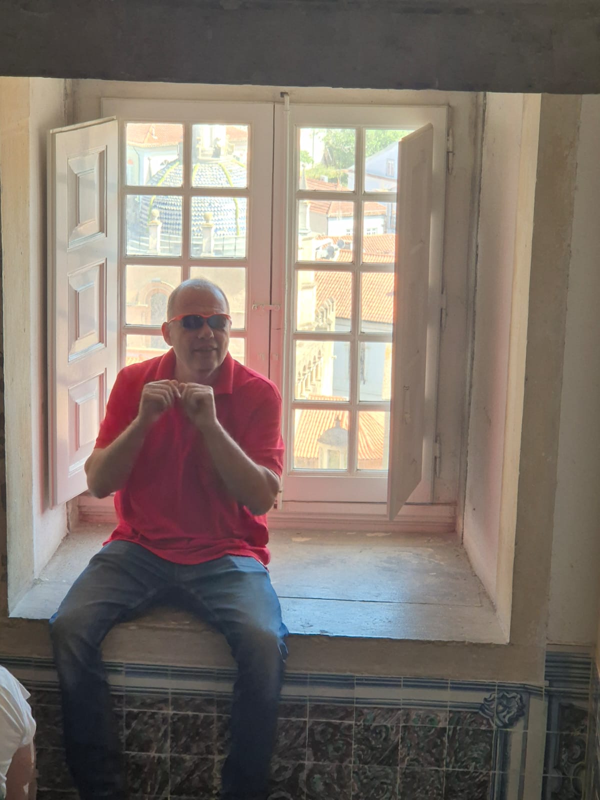 גיורא יושב על אדן חלון באוניברסיטת קוימברה, לבוש חולצה אדומה, משקיף על כיפת הקתדרלה והעיר העתיקה